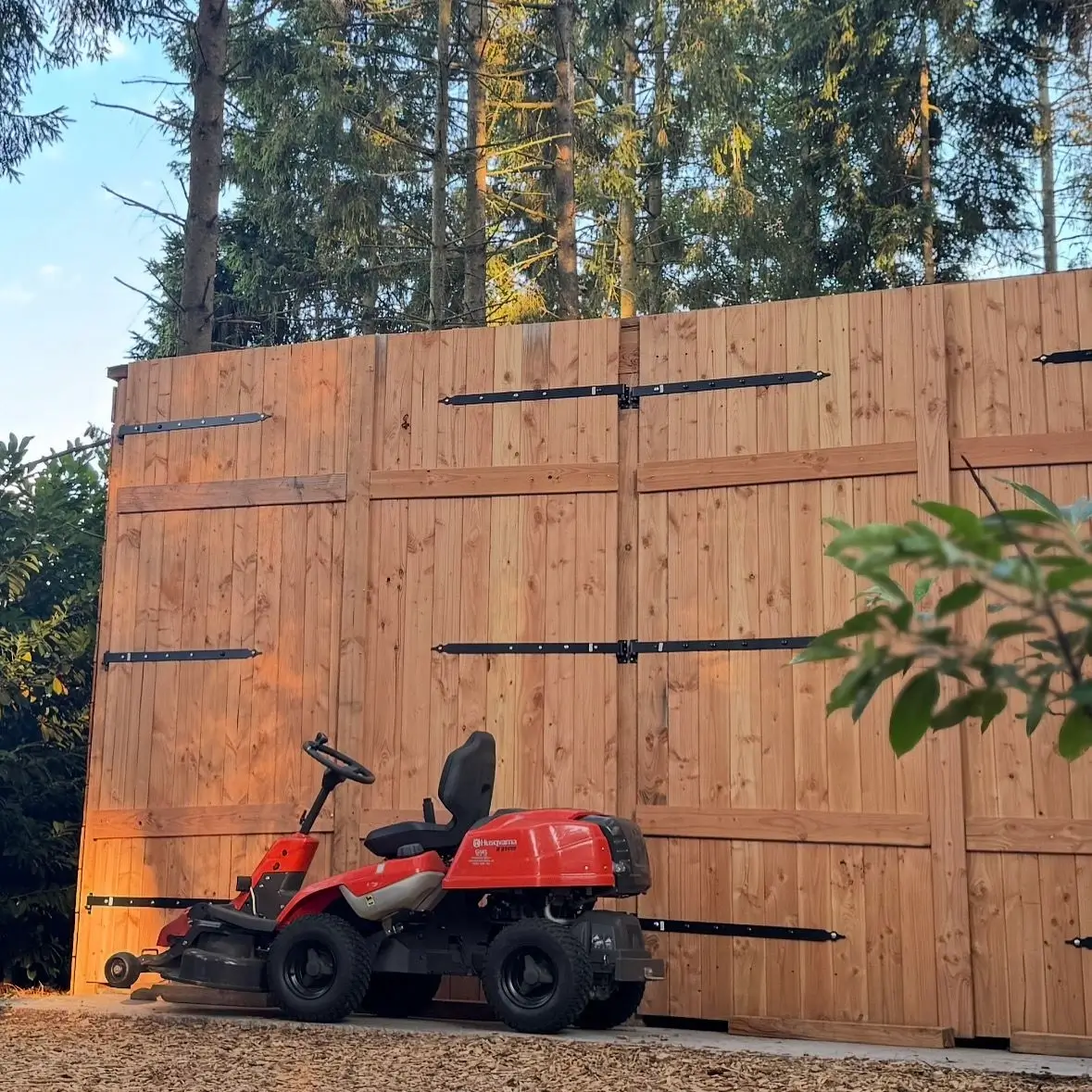 Een houten schuur met een grasmaaier ervoor.